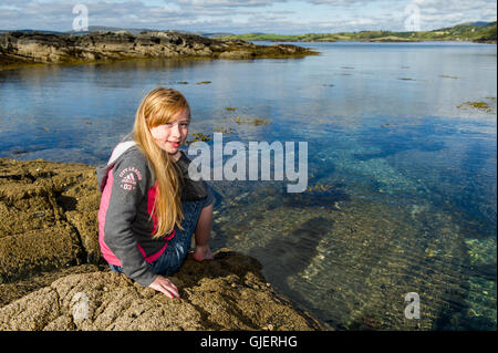 Une belle fille de 9 ans, assis sur des rochers en bord de mer à l'Ouest de Cork, Irlande avec copie espace. Banque D'Images