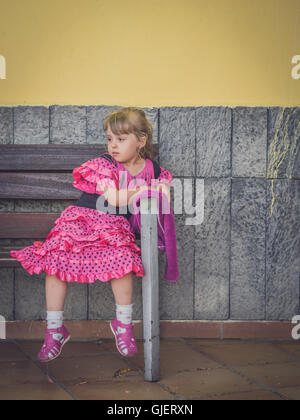 Sad girl habillé en robe rose assis seul sur un banc à l'extérieur de l'école de danse Banque D'Images