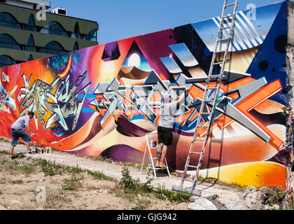 Graffiti artistes à l'œuvre en peinture d'un vieux mur, Friedrichshain, Berlin, Allemagne. Banque D'Images