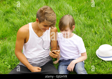 Plus vieux et plus jeune frère assis sur l'herbe et à la recherche au smartphone Banque D'Images