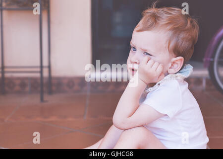 Boy sitting on floor with hand on chin Banque D'Images