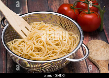 Spaghetti dans un boîtier en acier inoxydable sur une surface en bois collander Banque D'Images