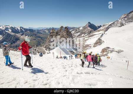 Les personnes équipées avec des casques de la descente d'une route dans la neige un jour d'été au glacier de Hintertux, Zillertal, Autriche Banque D'Images