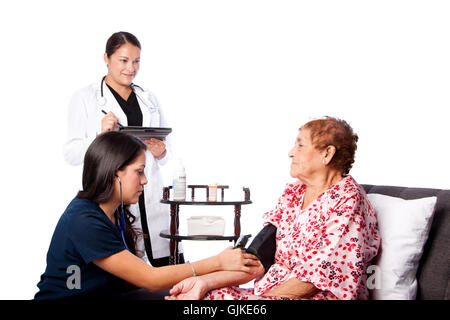 La mesure de la pression artérielle sur l'infirmière Senior woman alors que médecin, prend des notes. Banque D'Images