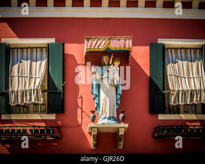 Statue de Vierge et d'enfant sur un mur extérieur de couleur terre cuite d'une maison traditionnelle sur l'île de Burano. Italie. Banque D'Images