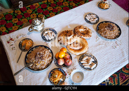 Le Kirghizistan, Jalabat : un dîner typique de l'Asie centrale, du riz avec de la viande, le thé vert, salade, fruits et des bonbons. Banque D'Images