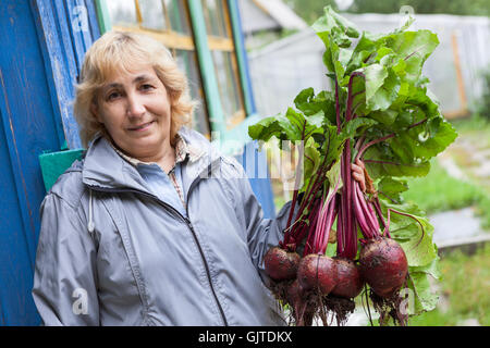 Happy woman standing près de maison d'été avec des betteraves en mains Banque D'Images