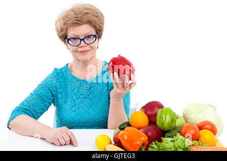 Aîné attrayant Caucasian woman showing poivron rouge, les légumes frais et les fruits sont sur la table, isolé sur blanc backgroun Banque D'Images