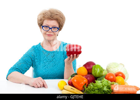 Portrait of senior woman showing poivron rouge dans la main alors qu'il était assis près de fruits et légumes frais, isolated on white background Banque D'Images