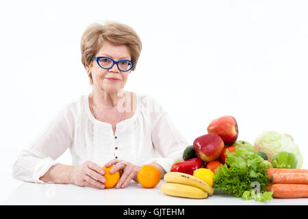 Aîné heureux Caucasian woman holding hands deux oranges, les légumes et les fruits sont sur la table, fond blanc Banque D'Images