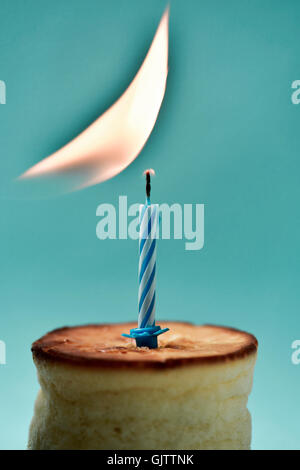 Libre d'un gâteau au fromage surmonté d'une bougie d'anniversaire qui est allumée, sur un fond bleu Banque D'Images