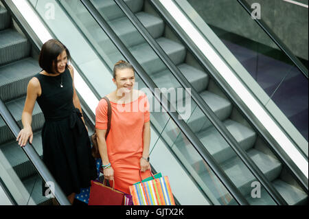 Deux belles jeunes copines sur l'escalator au centre commercial. Ils parlent de quelque chose. Les filles à la mode et habillé de couleurs vives. En h Banque D'Images