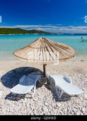 Parapluie de paille sur une plage de sable à la Grèce. Chaises de plage ...