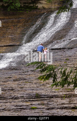 Sundell, Michigan - Un homme monte avec un petit enfant sur les roches humides adjacentes à rire Whitefish Falls. Banque D'Images