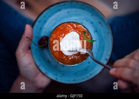 Mains tenant un verre de gâteau au fromage sans cuisson peach dans une plaque bleue. Banque D'Images