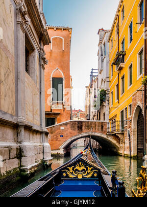 Canal étroit et petit pont voûté vu à partir d'une gondole, qui est dol fin est visible dans l'avant-plan. Venise, Italie. Banque D'Images
