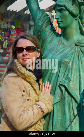 Une belle femme d'âge moyen avec des lunettes, les poses et les embrassades une miniature de la Statue de la liberté à côté d'une boutique touristique de la ville de New York Banque D'Images