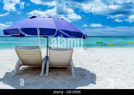 Une paire de chaises de plage sous un parasol sur une plage déserte avec du sable blanc. Banque D'Images