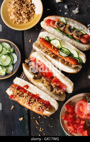 Assortiment de chiens chaudes faites maison avec de la saucisse, oignon frit, tomates et concombres, servi avec des ingrédients de différentes plaques sur Banque D'Images