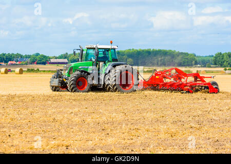 Kalmar, Suède - août 10, 2016 : le matériel roulant avec disque champ vert Fendt 820 tracteur. Ferme et forêt en arrière-plan. Banque D'Images
