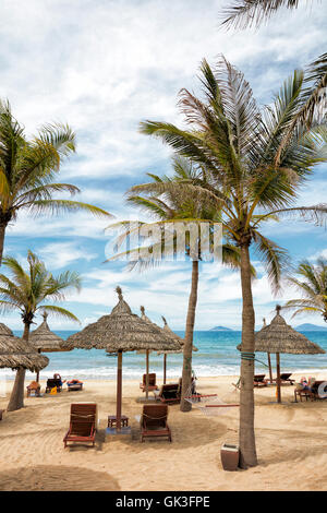 Chaises longues et parasols en chaume sous les palmiers sur la plage de Cua Dai. Hoi an, province de Quang Nam, Vietnam. Banque D'Images