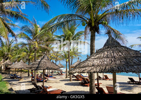 Des parasols en chaume sous les cocotiers sur la plage Cua Dai. Hoi An, Quang Nam Province, Vietnam. Banque D'Images