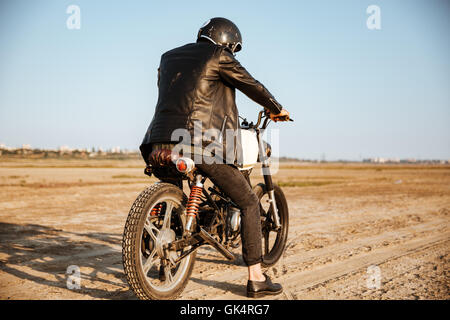 Vue arrière du jeune homme brutal dans une veste noire et de lunettes moto rétro de conduite Banque D'Images