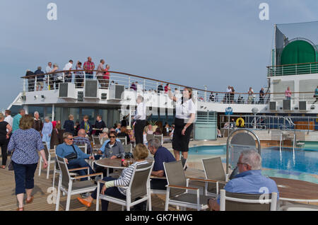 Deux stewards, un homme et une femme, le plomb le divertissement à bord du navire de croisière Arcadia alors qu'elle navigue loin de Southampton. Banque D'Images