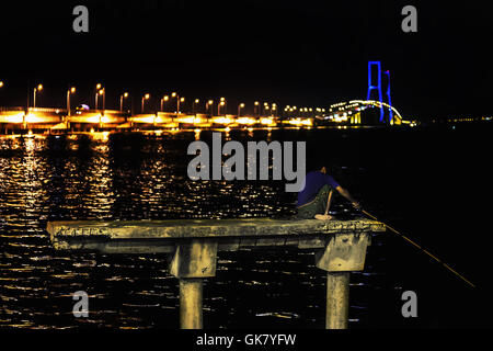 Pêcheur sur un pylône en béton pêcher de nuit. Backround dans Pont Suramadu au crépuscule du temps, Surabaya, Indonésie. Est la lo Banque D'Images