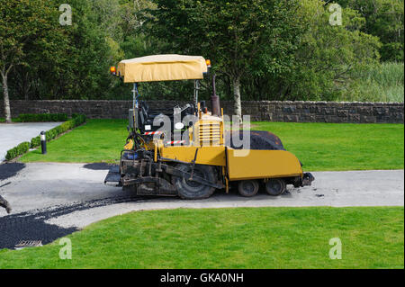 L'épandeur d'asphalte de couleur jaune avec la machine travaillant dans l'extérieur Banque D'Images