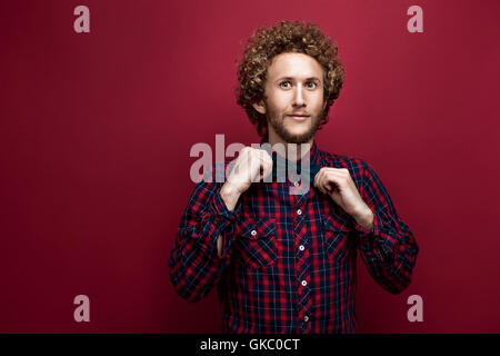 Portrait d'homme aux cheveux bouclés surpris en chemise à carreaux et Bow-tie sur fond rouge. Isoler Banque D'Images