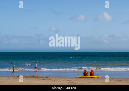 Une image sereine de plage de Tenby montrant deux sauveteurs, assis, gardant une montre sur le surf, les eaux et les nageurs Banque D'Images