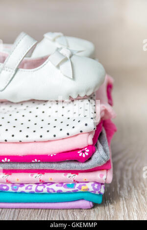 Body rose et blanc plié avec des chaussures sur elle sur fond de bois gris pour bébé fille nouveau-né.. Pile de vêtements pour bébé. Ch Banque D'Images