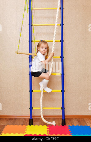 Petite fille monte les escaliers tenant à la corde. Mur de bars. Les appareils de sport. Sports pour enfants. Banque D'Images