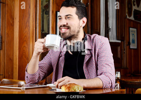 Portrait de jeune homme latin de boire du café avec un casque et tablette numérique dans un café. À l'intérieur. Banque D'Images