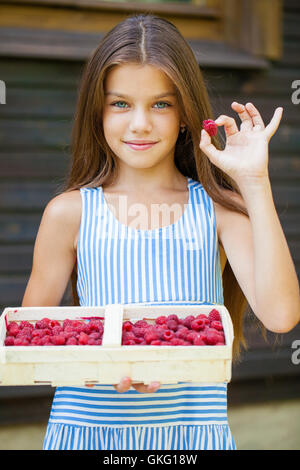 Belle brune petite fille tenant une boîte avec une framboise, été dehors Banque D'Images