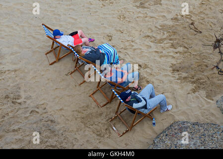 Les gens vous relaxant dans des chaises longues sur la plage, en Angleterre Banque D'Images