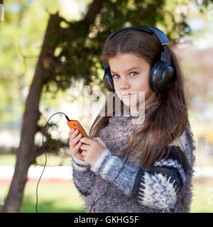 Belle petite fille listening to music on headphones in autumn park Banque D'Images