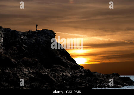 Homme marchant le long d'une falaise à Porth Dafarch, Anglesey, consulte une carte au coucher du soleil Banque D'Images