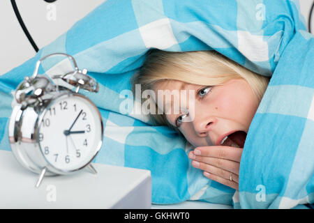 Jeune femme couchée dans le lit sans sommeil et à la recherche de l'horloge Banque D'Images