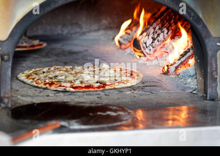 Jambon et ananas pizza à croûte mince la cuisson dans un four à pizza au feu de bois Banque D'Images