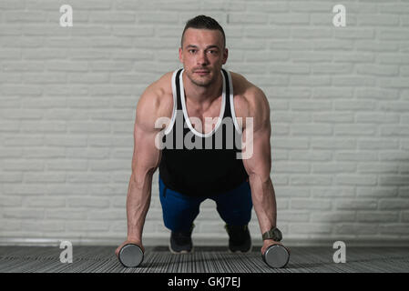 Jeune athlète faisant pompes avec haltères courtes dans le cadre de la formation de culturisme Banque D'Images