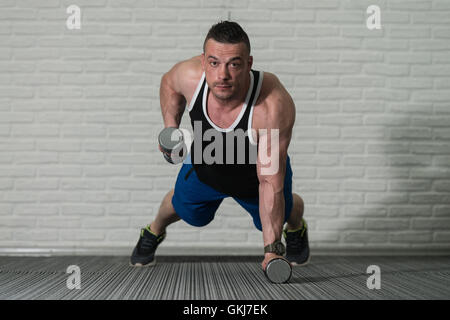 Jeune homme faisant pompes avec haltères courtes dans le cadre de la formation de culturisme Banque D'Images