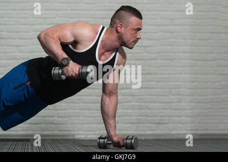 Jeune athlète faisant pompes avec haltères courtes dans le cadre de la formation de culturisme Banque D'Images