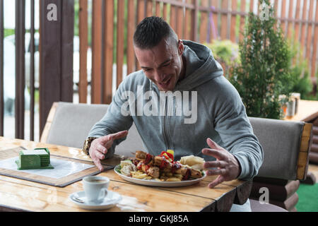 Portrait Of Happy Young Man Eating du poulet sur Stick servi avec riz sauvage au Restaurant Banque D'Images