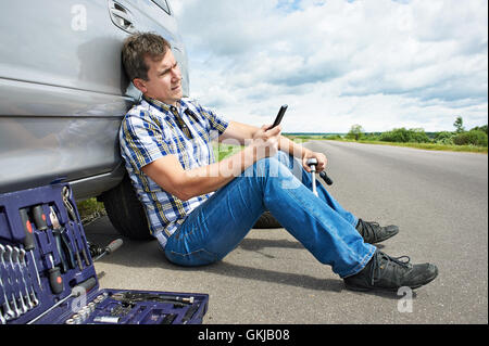 Homme avec téléphone est l'appel au service de pneu de rechange sa voiture Banque D'Images