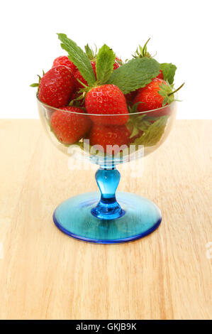 Fraises fraîches et de feuilles de menthe dans un verre sundae sur une table en bois sur un fond blanc. Banque D'Images