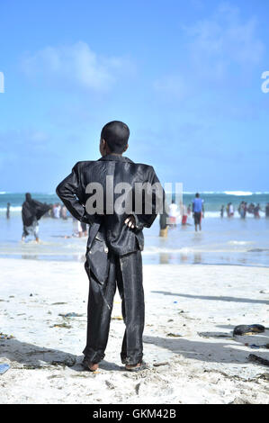 Un jeune garçon, vêtu d'un costume neuf pour l'Aïd, montres les gens jouent dans les vagues sur la plage du Lido à Mogadishu, Somalie, le 8 août. La Somalie aujourd'hui a été acquis à une solution pacifique Eid-Ul-Fitr, une des dates les plus importantes sur le calendrier musulman. Des milliers habillé et est sorti dans les rues pour profiter des vacances. PHOTO ONU / UA IST TOBIN JONES Banque D'Images