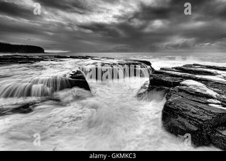 Seascape côtières escarpées spectaculaires près de Collaroy beach à Sydney au lever du soleil. Image noir et blanc de vagues de surf de miner les rochers Banque D'Images