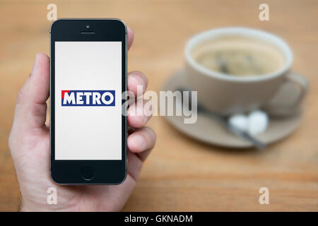 Un homme se penche sur son iPhone qui affiche le logo du métro, en restant assis avec une tasse de café (usage éditorial uniquement). Banque D'Images